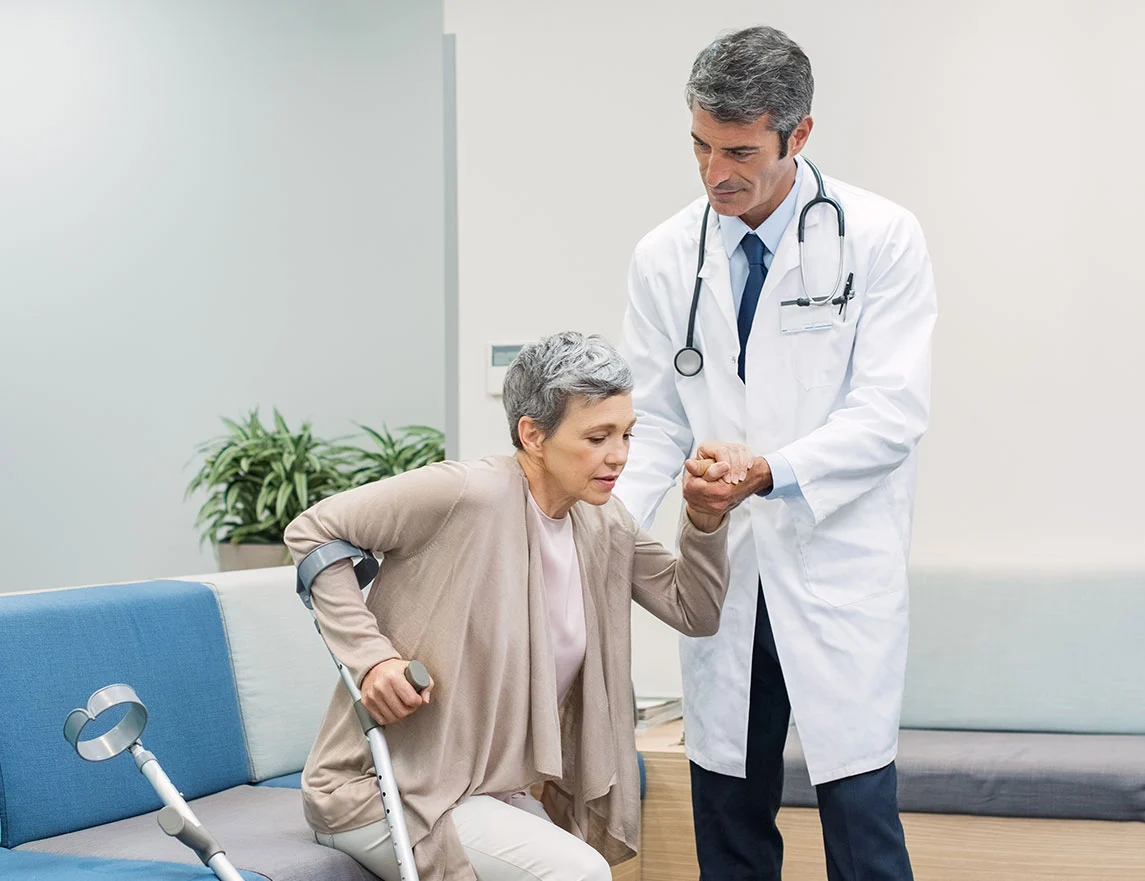 A doctor helps a woman with crutches get up from a waiting room seat. Clarkson Pennington Law disability attorneys help you prepare for the Social Security Disability application process.