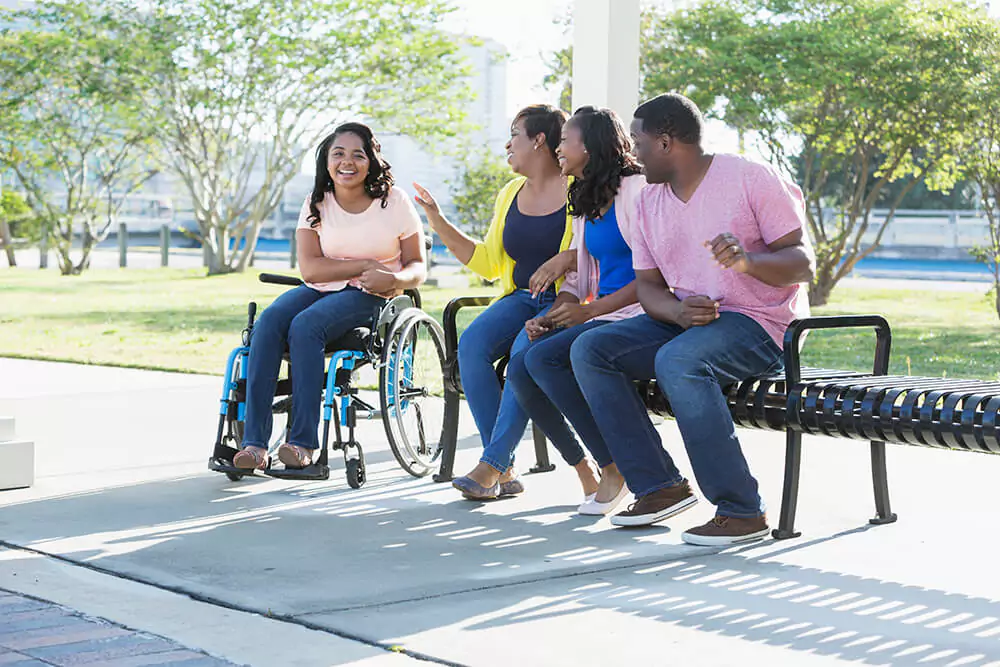 Three people sit on a park bench next to a woman in a wheelchair, all of them laughing and smiling. Clarkson Pennington Law disability attorneys can answer questions about getting Social Security Disability benefits.
