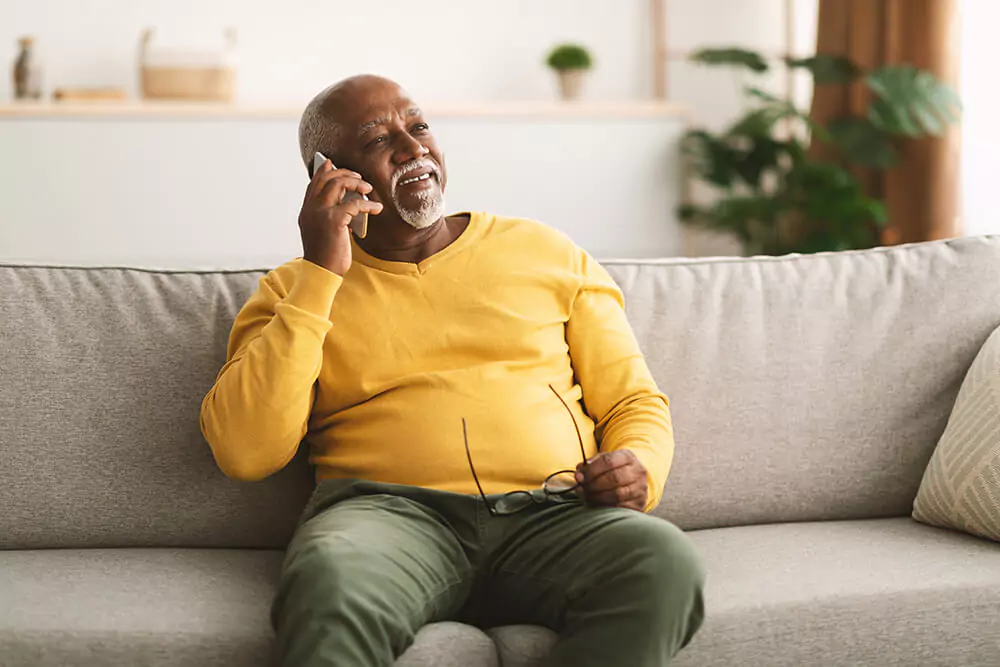 Holding his glasses in his lap, a man sits on a couch, talks on the phone and smiles. Clarkson Pennington Law Birmingham disability law provides the personal care and attention you deserve.