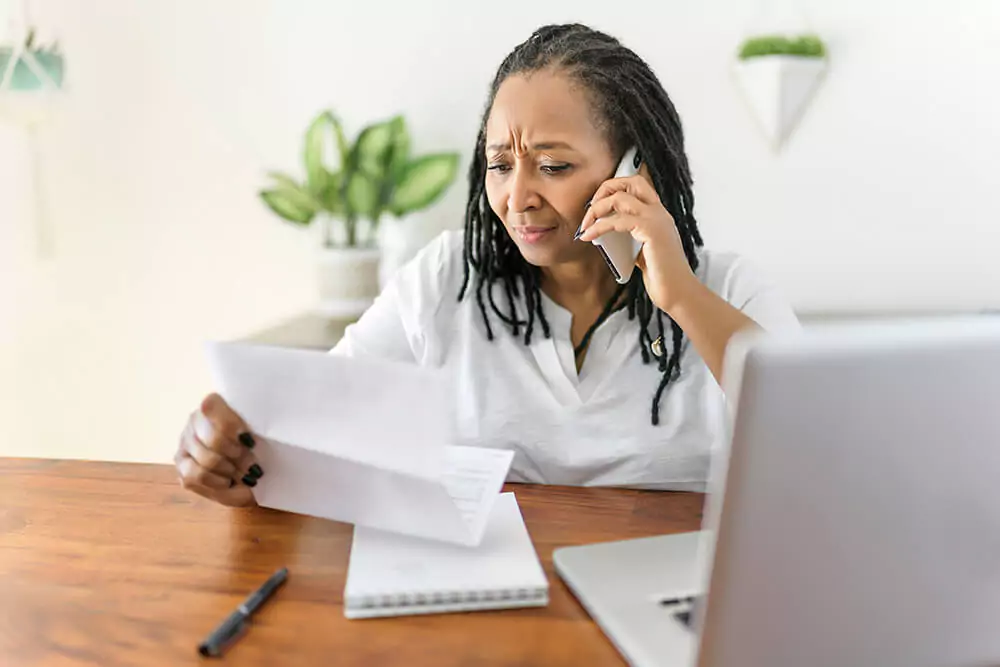 With a concerned expression, a woman sits at a dining room table and talks on the phone while looking at a sheet of paper. Clarkson Pennington Law disability attorneys help you prepare for the Social Security Disability application process.